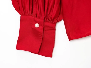 Macro detail of red long sleeve cuff with pleated texture and white pearl button