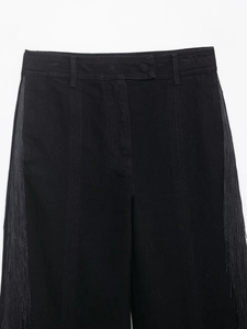 Détail du jean noir à taille haute avec de franges denses sur les coutures latérales