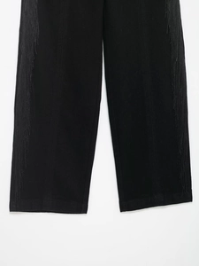 Détail du pantalon droit noir avec des finitions à franges longues sur les côtés