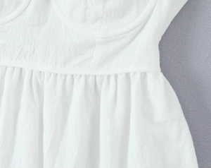 Close-up of white dress showing textured crinkle fabric and corset-style waist stitching
