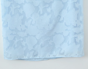 Macro detail of light blue sheer fabric featuring elegant rose floral jacquard patterns