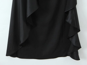 Detail of elegant black satin dress featuring asymmetrical ruffled hem and glossy texture