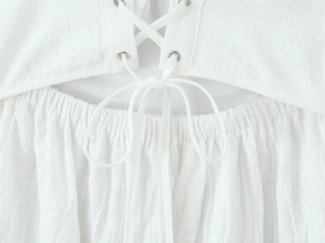 Detail of white lace dress featuring criss-cross lacing, metal eyelets and smocked waist