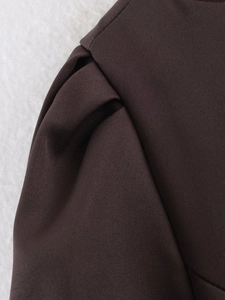 Makro-Detail des dunkelbraunen Kleiderstoffs mit aufwendiger Plissee-Schulternaht-Textur