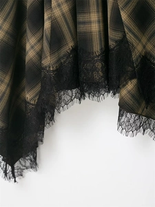 Detailed view of green plaid fabric with black eyelash lace trim on an asymmetric hem