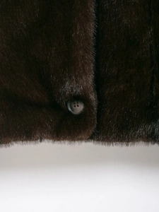 Detailed macro shot of dark brown faux fur texture and a polished round button on coat