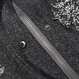 Macro view of floral sequin embroidery and metal zipper on grey wool jacket