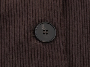 Detail of dark brown corduroy fabric with a secure black four-hole button on the blazer