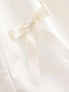 Macro shot of white satin fabric with a delicate bow detail and silky smooth texture