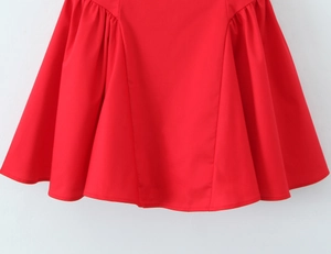 Detail of red sleeveless dress hem featuring pleated design and woven fabric texture