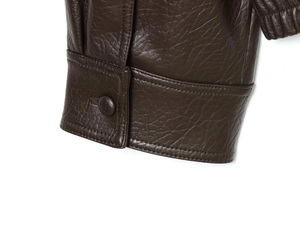 Détail de la manchette d'une veste en similicuir marron foncé avec bouton et couture