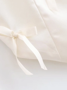 Detailed view of the elegant satin bow accent on a cream-colored backless halter top