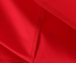 Macro shot of high-quality flatlock stitching and hem detail on red woven fabric dress