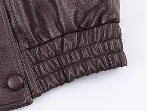 Détail de l'ourlet élastique et du bouton gainé de cuir sur une veste en PU marron