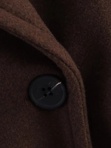 Close-up of a black button on high-quality dark brown wool fabric of a long winter coat