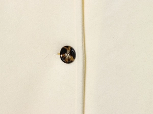Detailed close-up of dark marble texture button on a cream-colored wool coat fabric