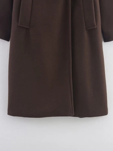Detail view of deep chocolate wool coat hem showing heavy fabric texture and pocket flap