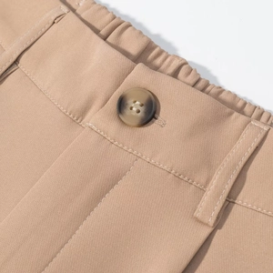Detail of khaki trousers featuring elastic back waistband, resin button, and neat stitching
