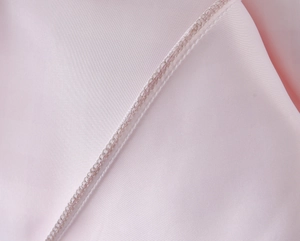 Close-up of the fine stitching and rolled hem on the light pink satin puff dress fabric