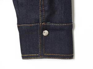 Detailed macro view of dark blue denim cuff with orange stitching and silver metal button
