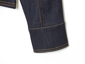 Detail of dark blue denim cuff with orange contrast stitching and high-quality texture