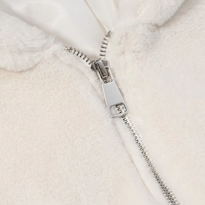 Détail de la fermeture éclair en métal argenté sur veste en peluche blanche et doublure soyeuse