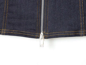 Detailed close-up of metal zipper and yellow stitching on dark blue denim jacket fabric