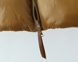 Detail of caramel puffer jacket featuring a matching color zipper and ribbon puller