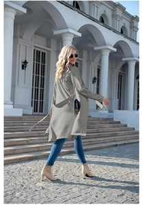 Outdoor street view of a grey long-sleeved midi trench coat with adjustable waist tie