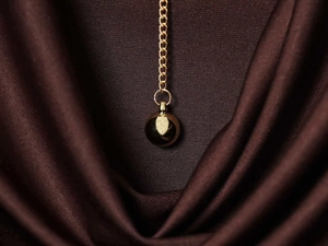 Macro shot of gold chain necklace with round metallic sphere pendant on silk fabric
