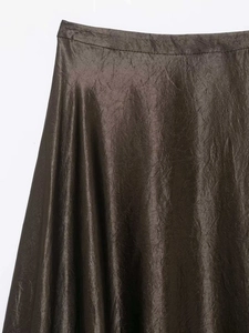 Détail d'une jupe en satin bronzé montrant la texture plissée et l'éclat de la soie