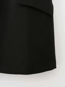 Detail of the black blazer dress showing a clean woven texture and flap pocket stitching