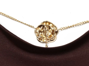 Macro detail of a 3D layered rose pendant in polished gold plating with a fine chain