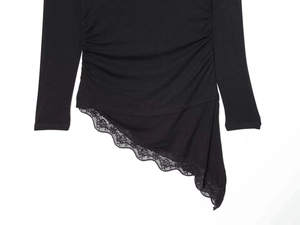 Detail of black knit top featuring ruched sides, asymmetric hem, and delicate lace trim