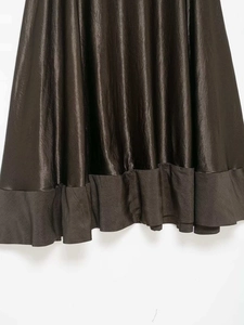 Détail d'une jupe en satin avec texture plissée et ourlet volanté en bronze