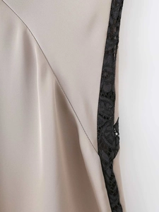 Detailed close-up of champagne satin fabric and intricate black lace stitching on dress
