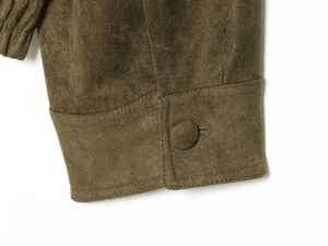 Nahaufnahme der olivgrünen Wildlederjacke mit stoffbezogenem Knopf und feinen Nähten