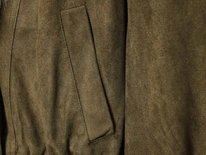 Detailaufnahme einer olivgrünen Wildlederjacke mit Taschenklappe und Ziernähten