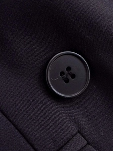 Detailed close-up of a matte black four-hole button on textured woven fabric blazer