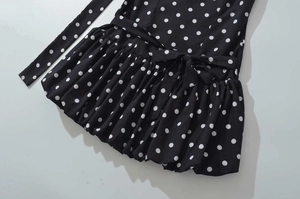 Close-up of black polka dot mini dress featuring a waist bow tie and pleated skirt detail