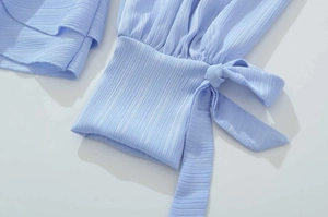 Detail of light blue puff sleeve dress showing textured fabric and a decorative bow tie cuff