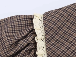 Detailed close-up of vintage brown plaid fabric with beige lace trim and pleats