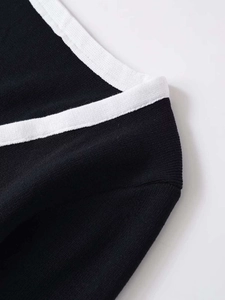 Detail shot of black knit cardigan featuring contrasting white trim and fine ribbed texture
