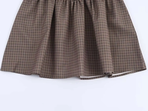 Detail of vintage brown plaid dress fabric showing pleated texture and checkered pattern