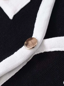 Detail of a gold metallic button on a black knit cardigan with white trim borders