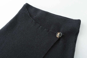 Macro detail of black ribbed knit skirt featuring a stylish amber button and overlap closure