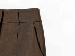 Detailed view of dark brown wool trousers with waist pleats and side pockets