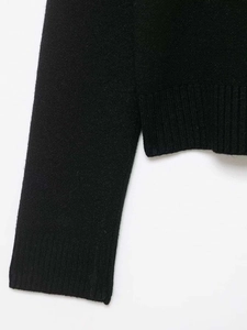 Détail d'un pull en maille noire montrant des poignets côtelés et des fentes latérales