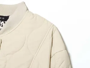Detail of quilted beige bomber jacket collar with ribbed neckline and polka dot lining