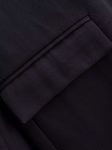 Detailed close-up of a flap pocket on a black woven dress showing high-quality stitching